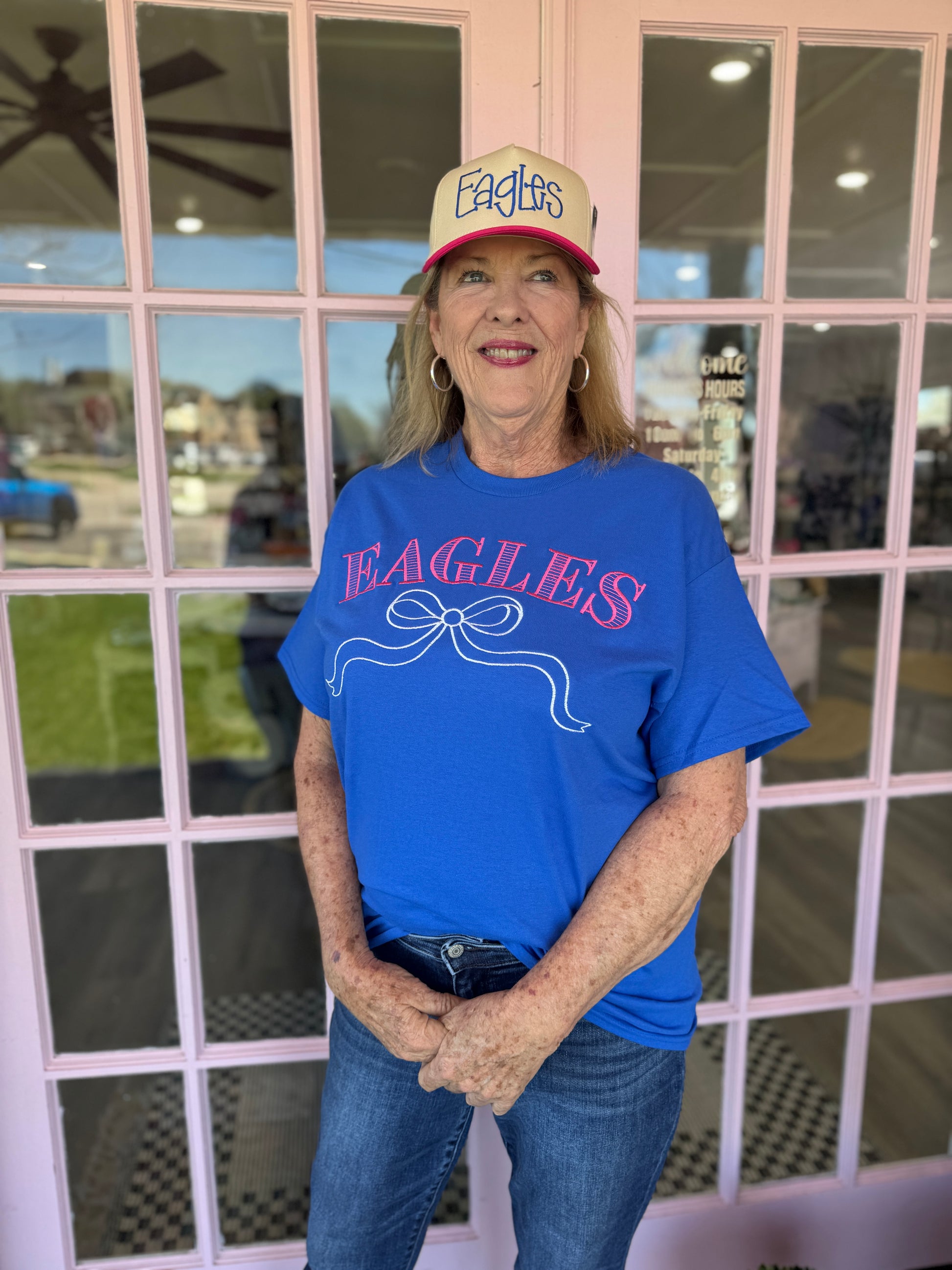 Person wearing a blue 'Eagles' shirt and cap standing in front of a window.