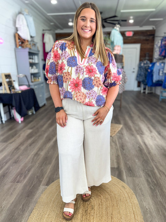 Woman wearing a colorful floral blouse and white pants in a store setting
