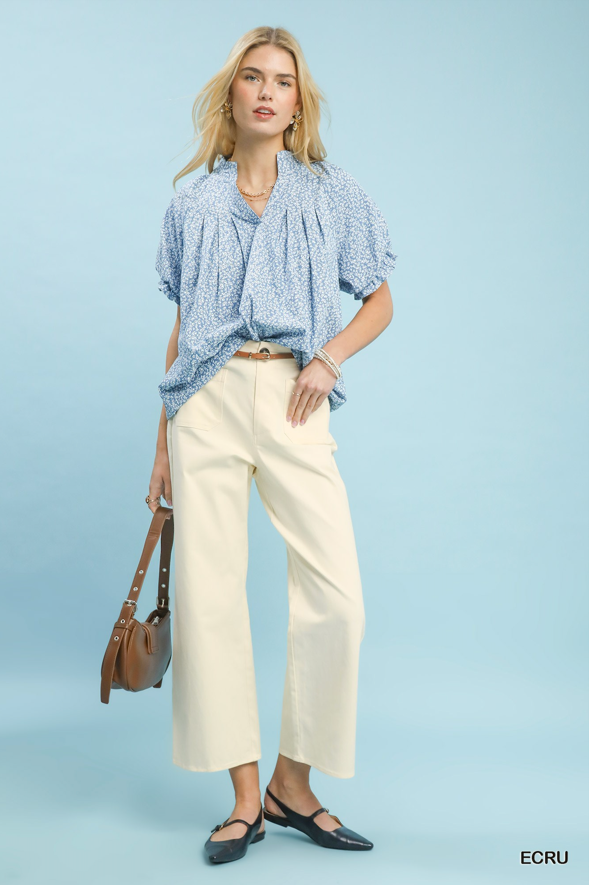 Women wearing a blue and white blouse with ecru colored pants on a light blue background.