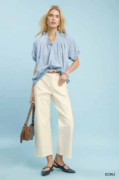 Women wearing a blue and white blouse with ecru colored pants on a light blue background.