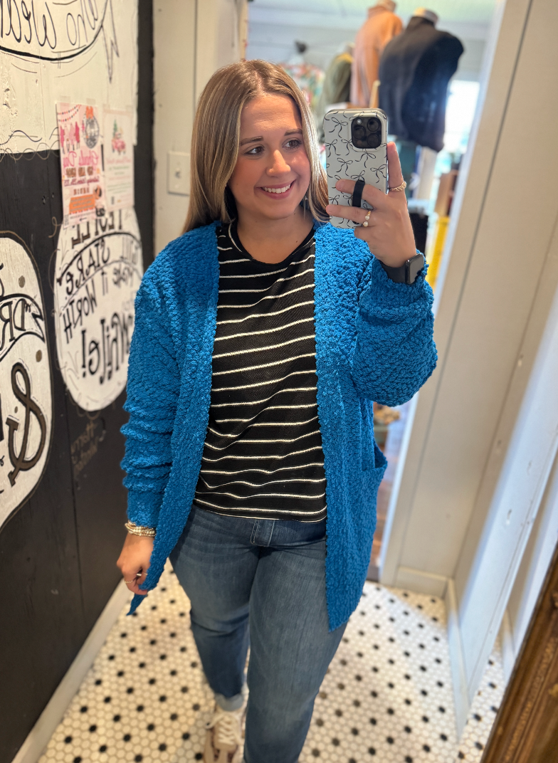 Woman taking a mirror selfie wearing a blue cardigan, striped shirt, and jeans.
