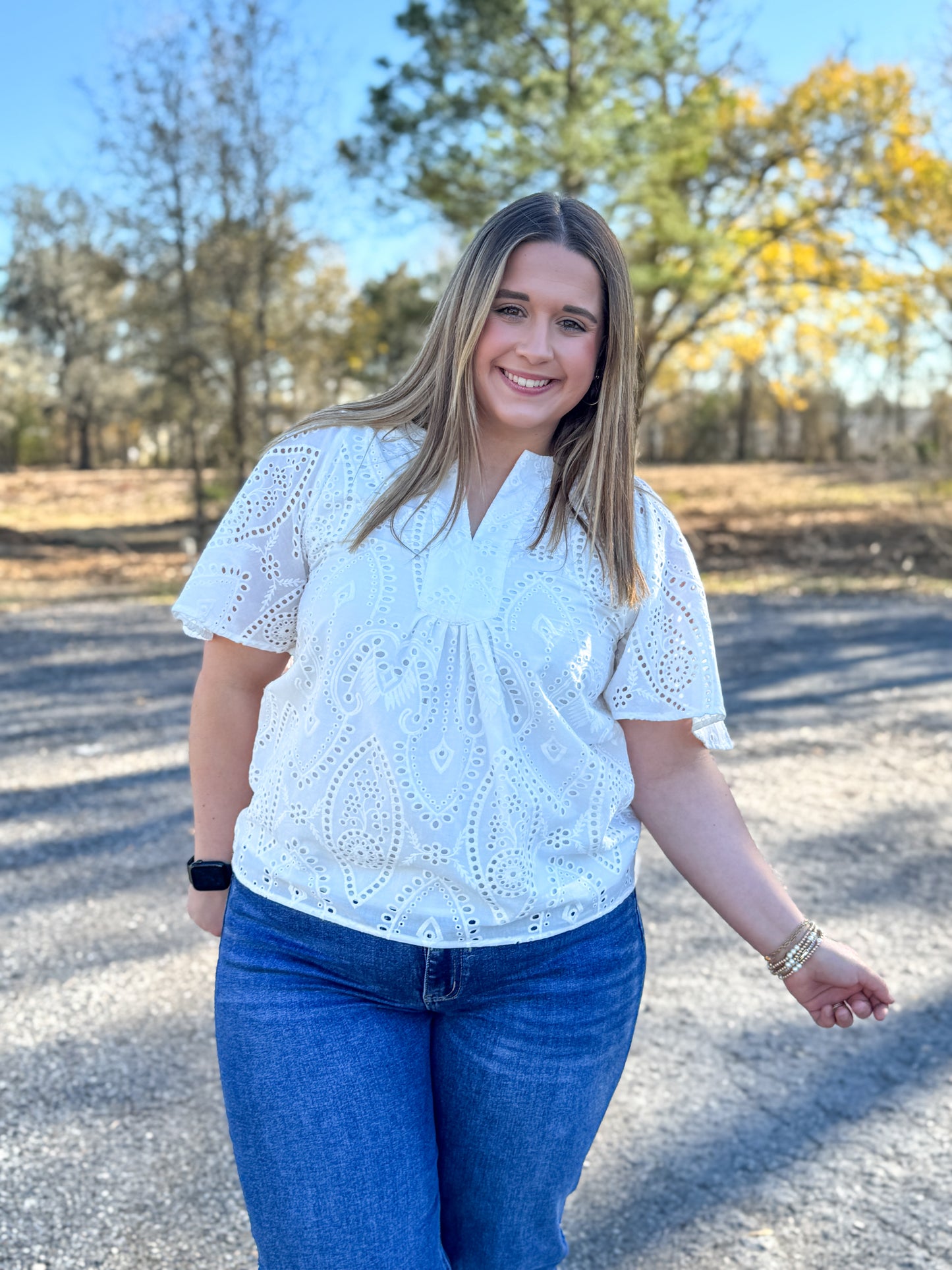 Woman wearing a white blouse with short sleeves and blue jeans standing outdoors.