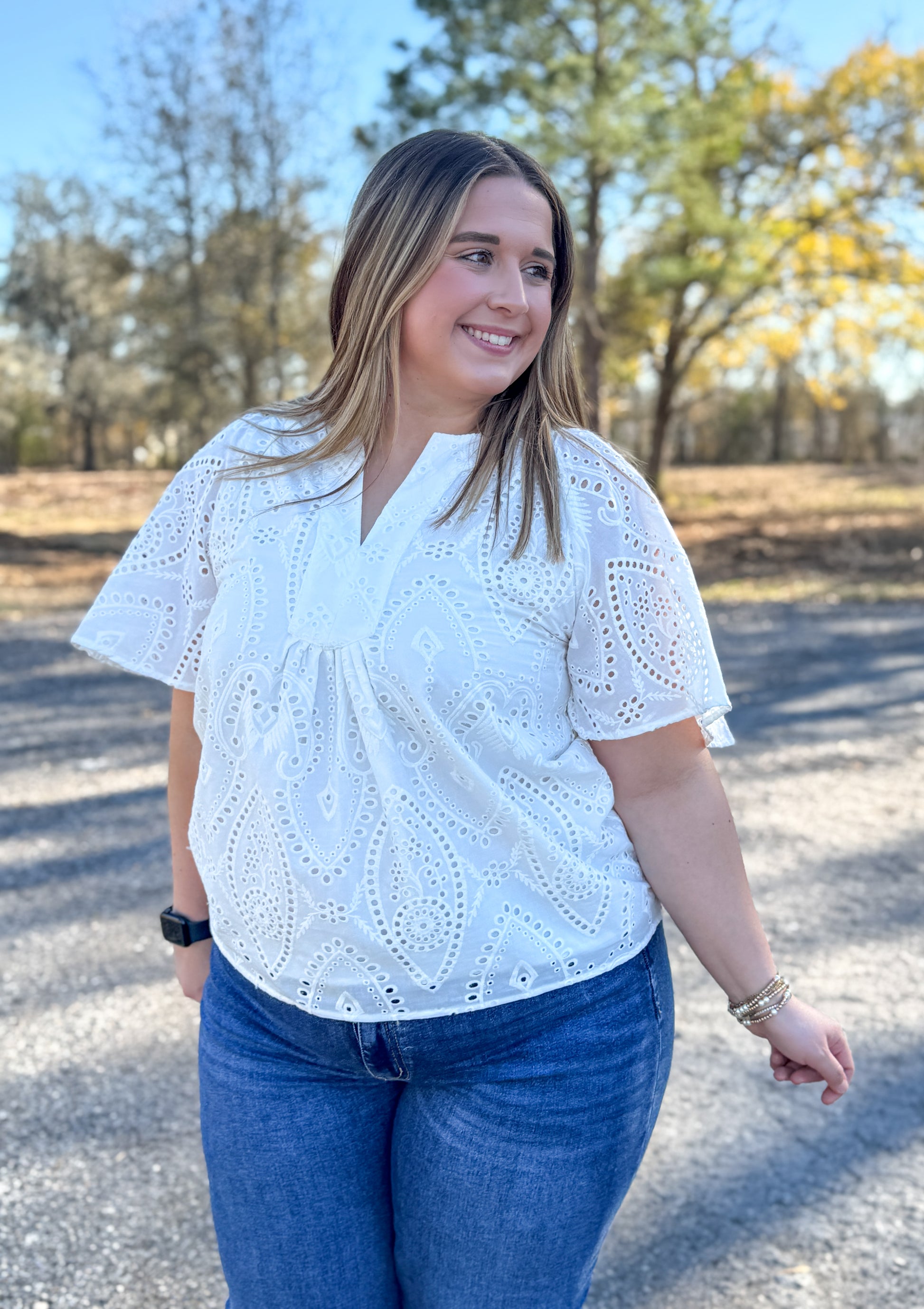 Woman wearing a white blouse with short sleeves and blue jeans standing outdoors.