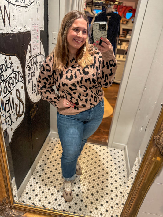 Woman taking a mirror selfie wearing a leopard print sweater and blue jeans in a store.