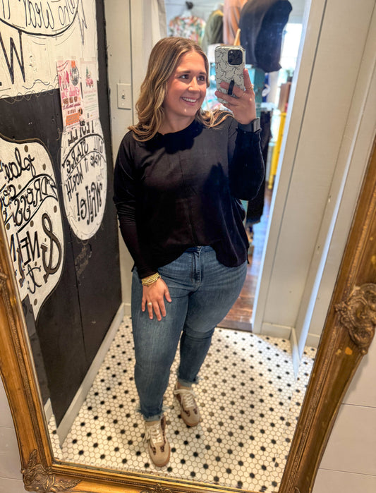 Woman taking a mirror selfie wearing a black sweater and blue jeans in a store.