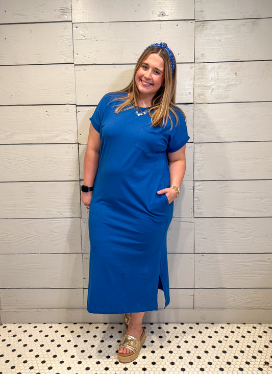 Woman wearing a blue dress standing against a wooden paneled wall.