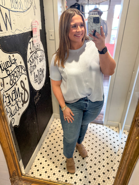 Woman taking a mirror selfie wearing a white top and blue jeans in a room with decorative elements.