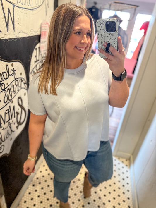 Woman taking a mirror selfie wearing a white top and blue jeans in a room with a decorative wall.