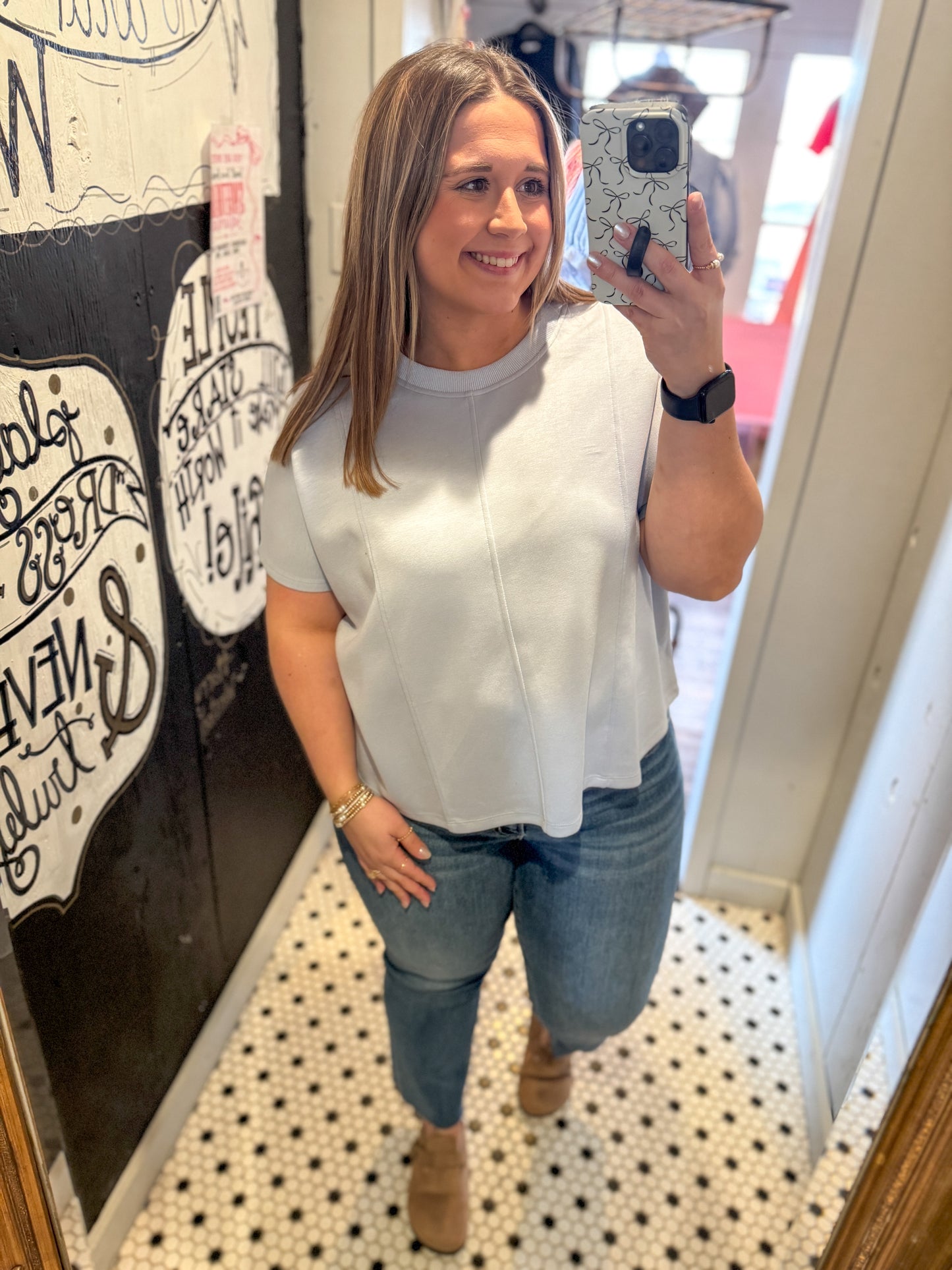 Woman taking a mirror selfie wearing a white top and blue jeans in a store.