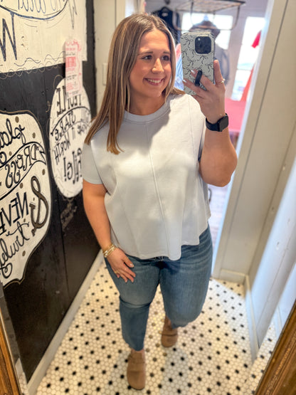 Woman taking a mirror selfie wearing a white top and blue jeans in a store.