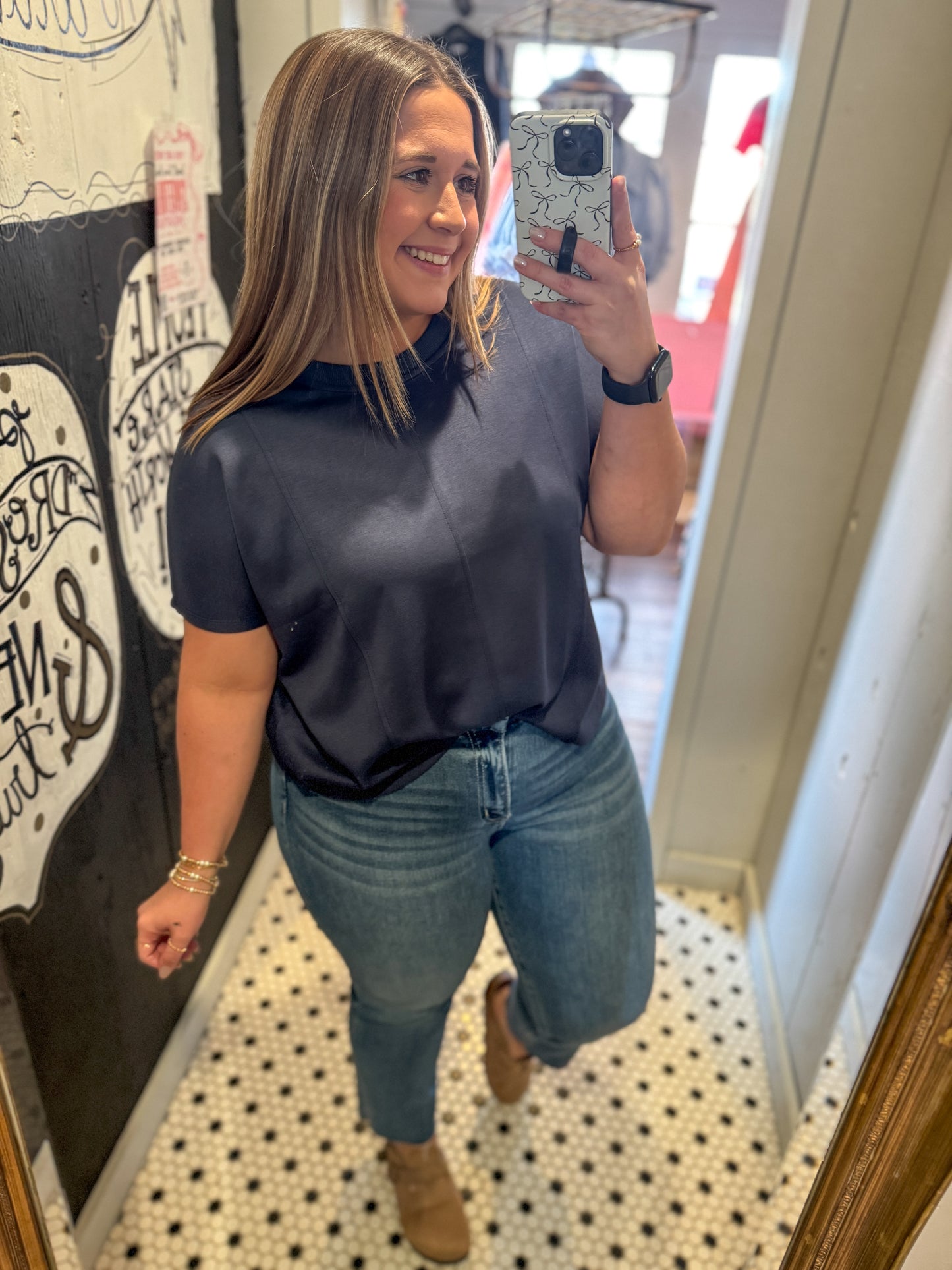 Woman taking a mirror selfie wearing a dark blue top and jeans in a room with decorative elements.