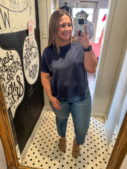 Woman taking a mirror selfie wearing a navy blue top and jeans in a room with decorative elements.