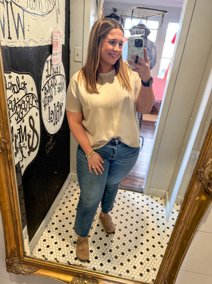Woman taking a mirror selfie wearing a beige top and blue jeans in a room with decorative elements.