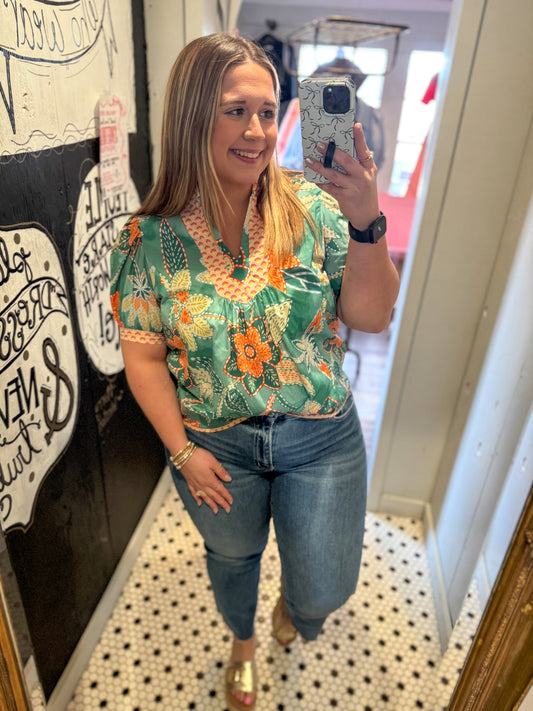 Woman taking a mirror selfie wearing a floral top and jeans.