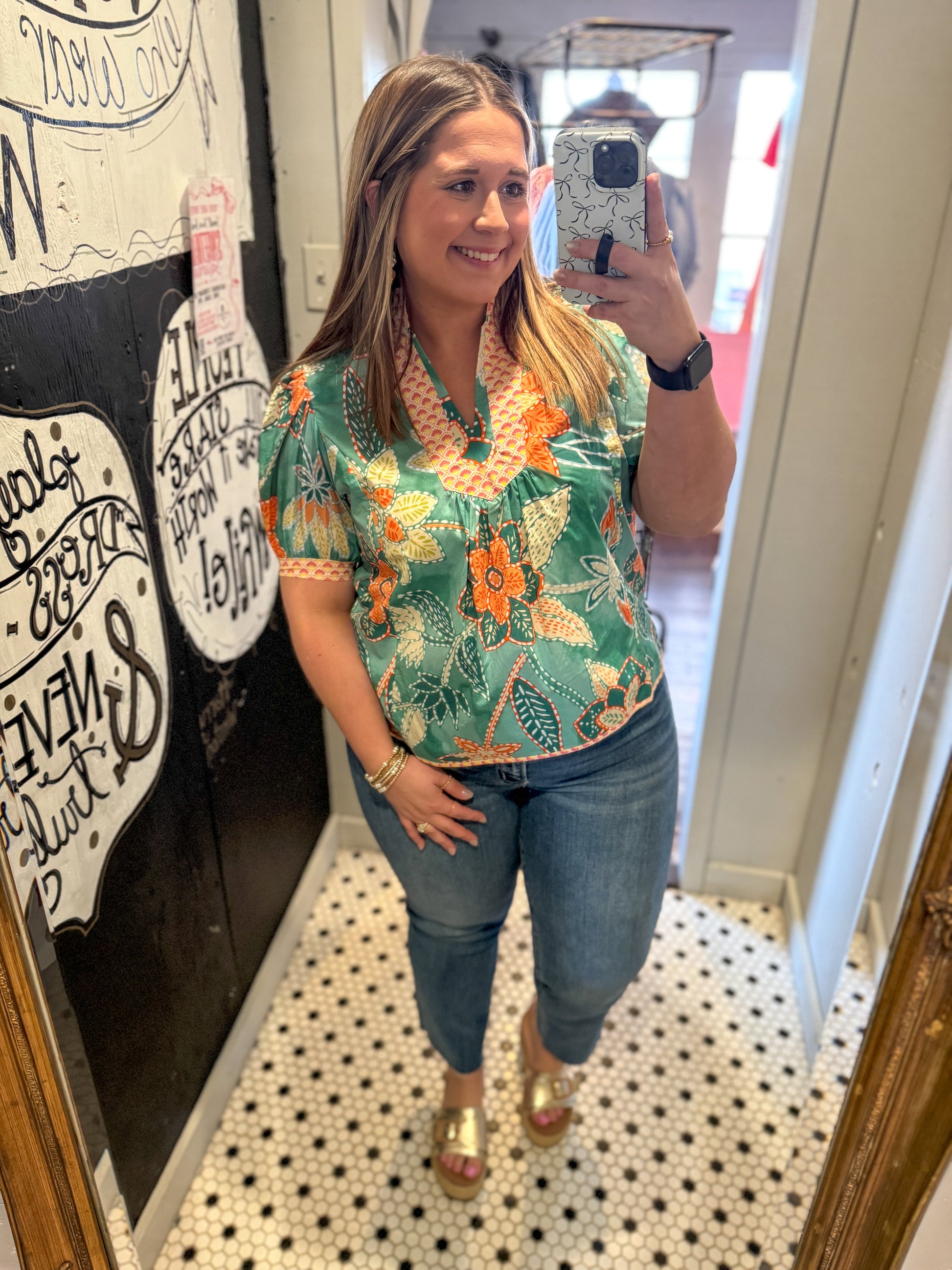 Woman taking a mirror selfie wearing a floral blouse and jeans in a store.