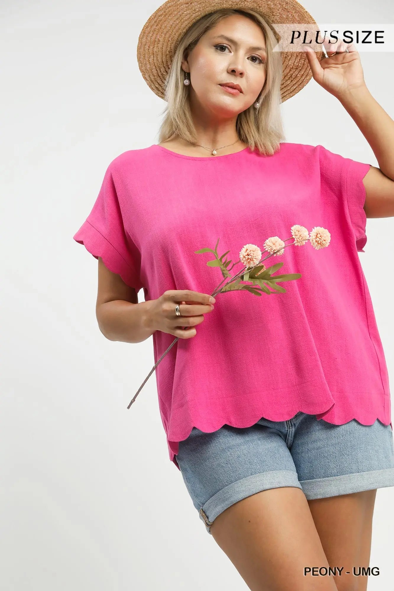 Woman wearing a pink blouse with floral design and denim shorts on a white background