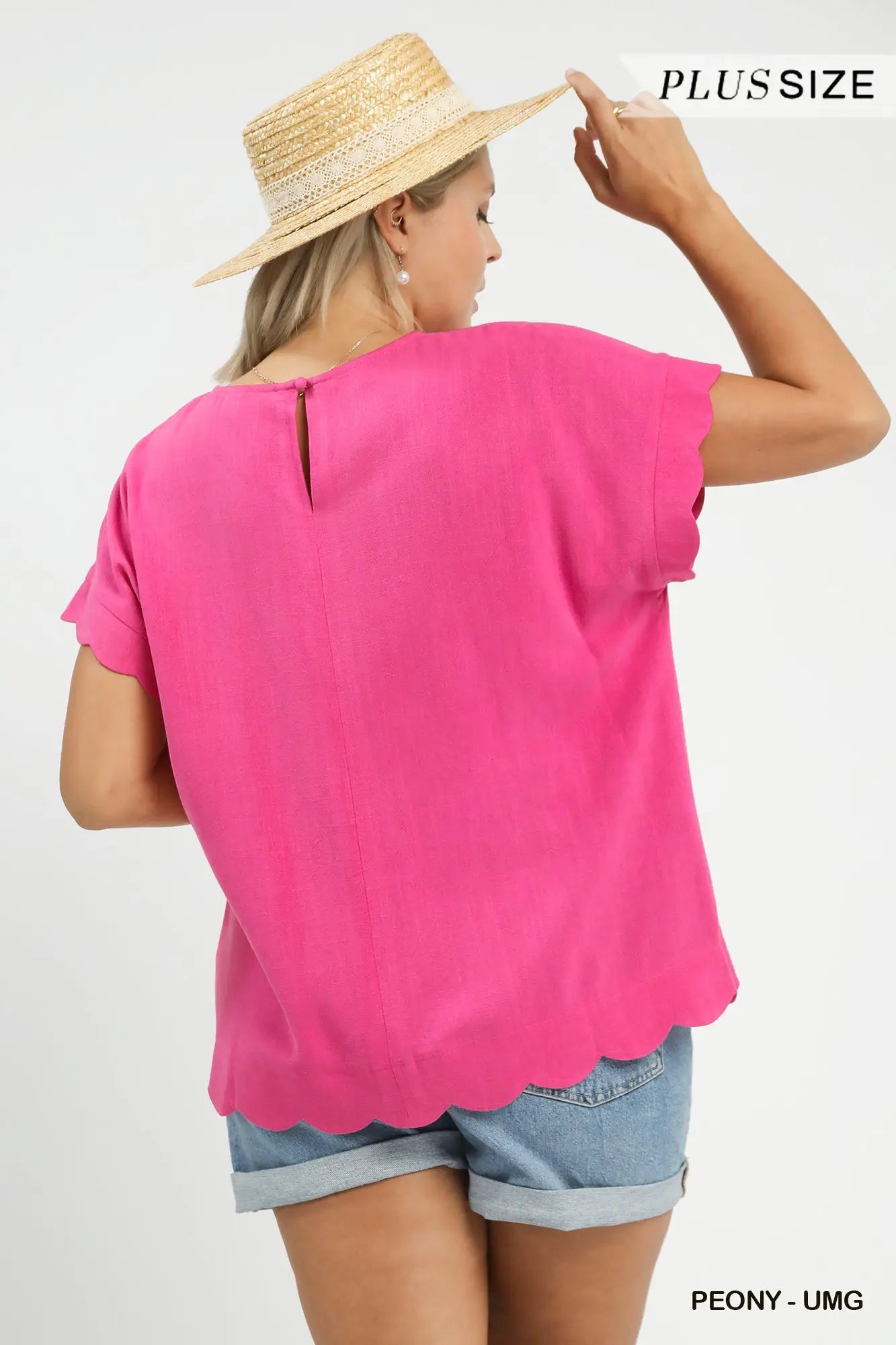 Woman wearing a bright pink top and denim shorts with a straw hat on a white background