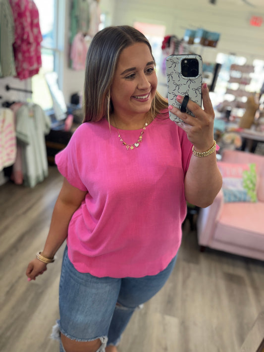 Woman taking a mirror selfie wearing a pink top and denim shorts in a store.