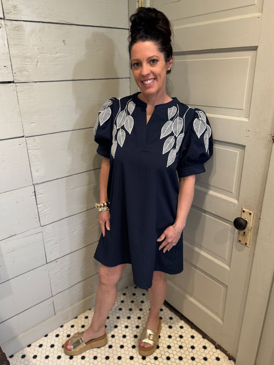 Woman wearing a navy dress with leaf patterns in a bathroom setting