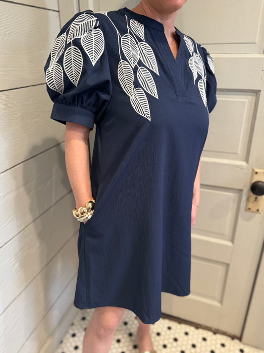 Person wearing a navy dress with white leaf patterns in a bathroom setting