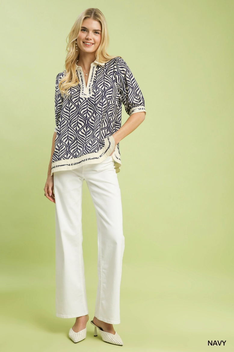 Woman wearing a navy patterned blouse and white pants on a light green background