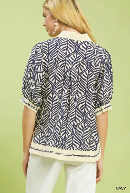 Woman wearing a navy patterned shirt with white pants on a light green background