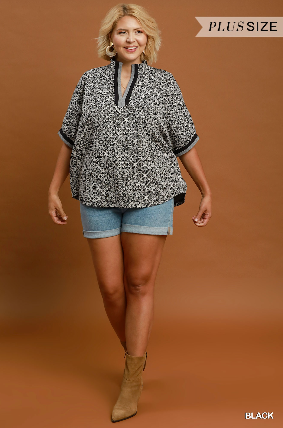 A woman modeling a black and white geometric patterned short-sleeve blouse with black trim, paired with denim shorts and tan ankle boots, against a solid brown studio background. A 'PLUS SIZE' banner is visible in the top right, and 'BLACK' is written in the bottom right.
