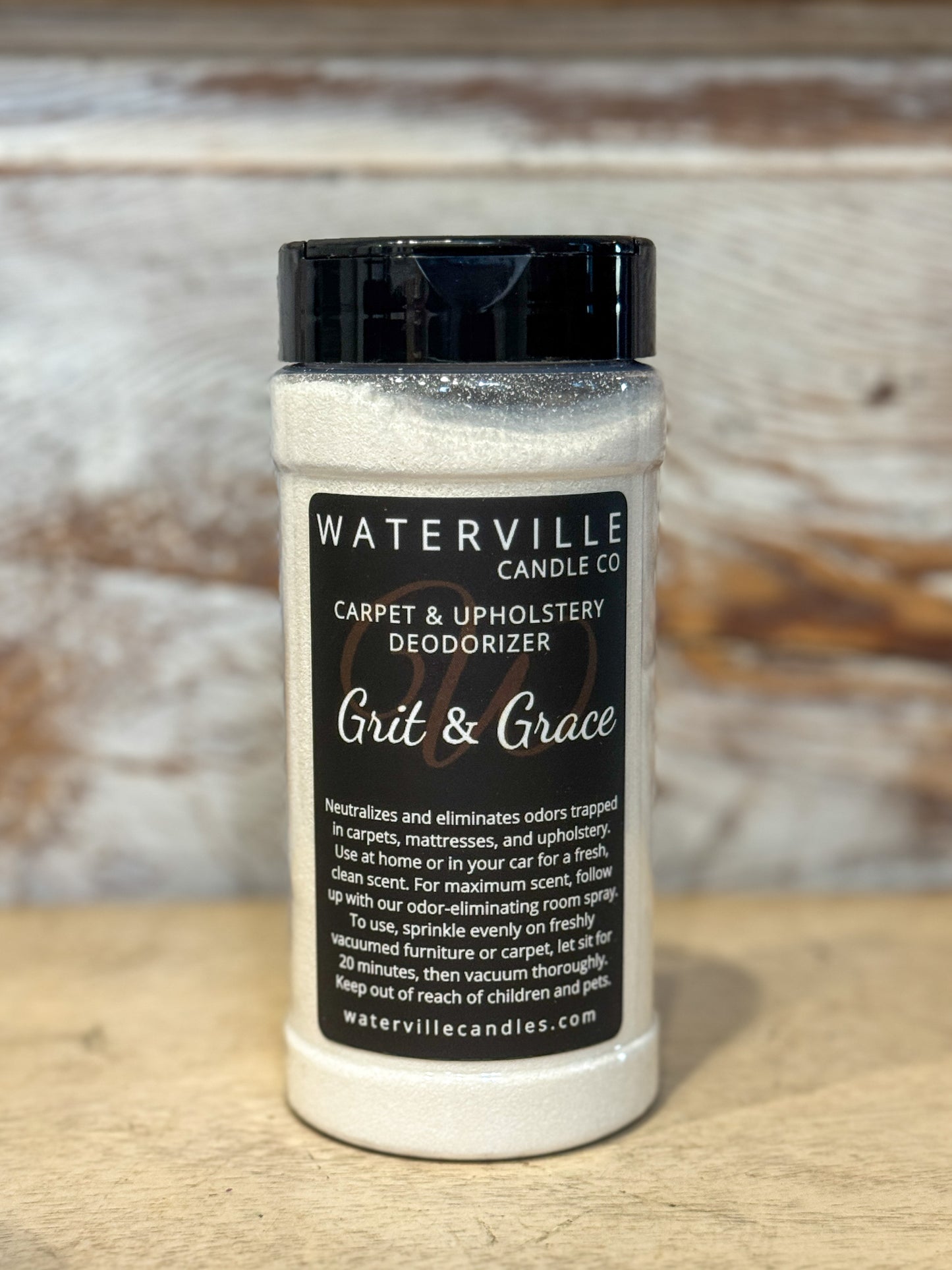 Bottle of Waterville Candle Co. carpet and upholstery deodorizer on a wooden surface with a rustic background.