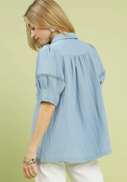 Woman wearing a light blue blouse with ruffled sleeves against a light green background