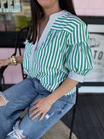 Person wearing a green and white striped shirt and blue jeans sitting on a chair.