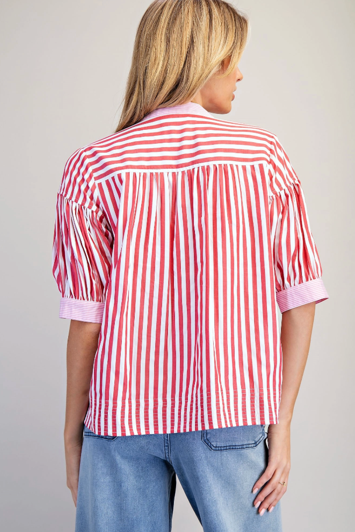 Person wearing a red and white striped shirt with rolled-up sleeves on a plain background