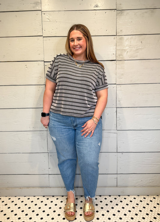Woman wearing a striped shirt and jeans standing against a wooden wall.