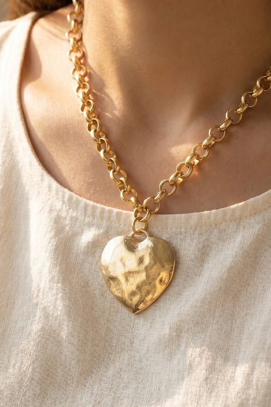 Gold chain necklace with a heart pendant worn by a person on a light background