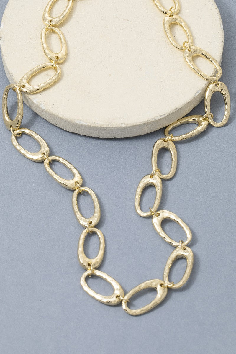 Gold chain necklace on a white round stand with a light gray background