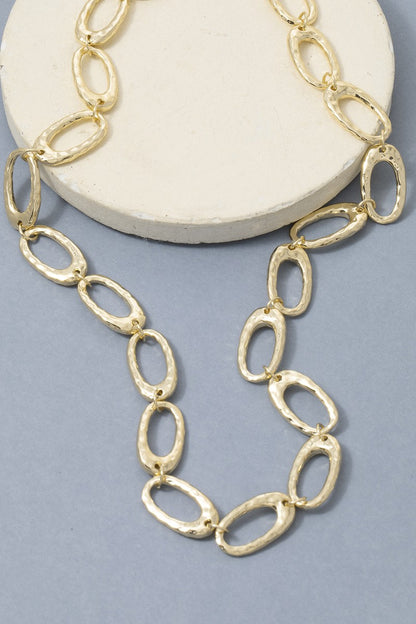 Gold chain necklace on a white round stand with a light gray background