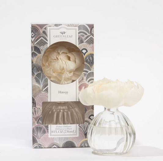 Greenleaf Haven reed diffuser set featuring a patterned box with a window showing a cream-colored reed flower, alongside a clear glass reed diffuser bottle filled with water and topped with the same cream reed flower, on a white background.