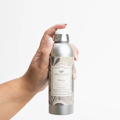 A hand holding a silver spray bottle of Greenleaf London Haven Herbal Mist against a clean white background.