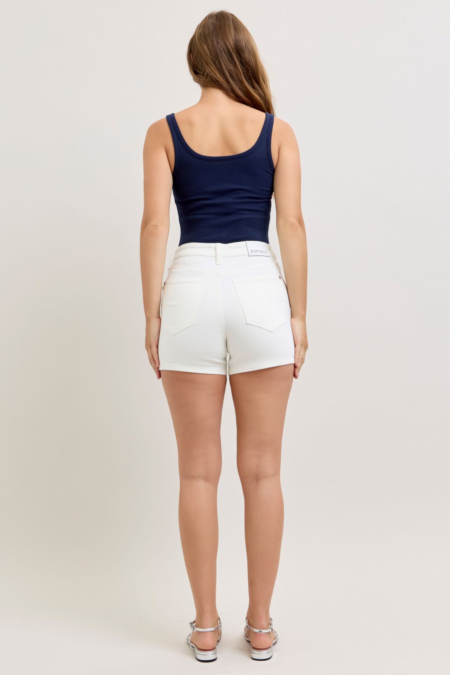 Person wearing a navy tank top and white shorts on a plain background