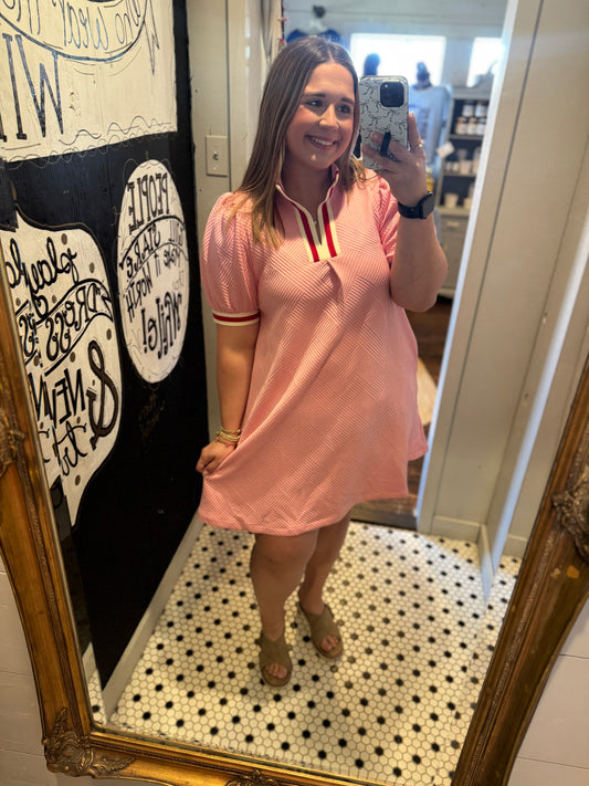 Woman taking a mirror selfie wearing a pink dress with a decorative wall and floor in the background.