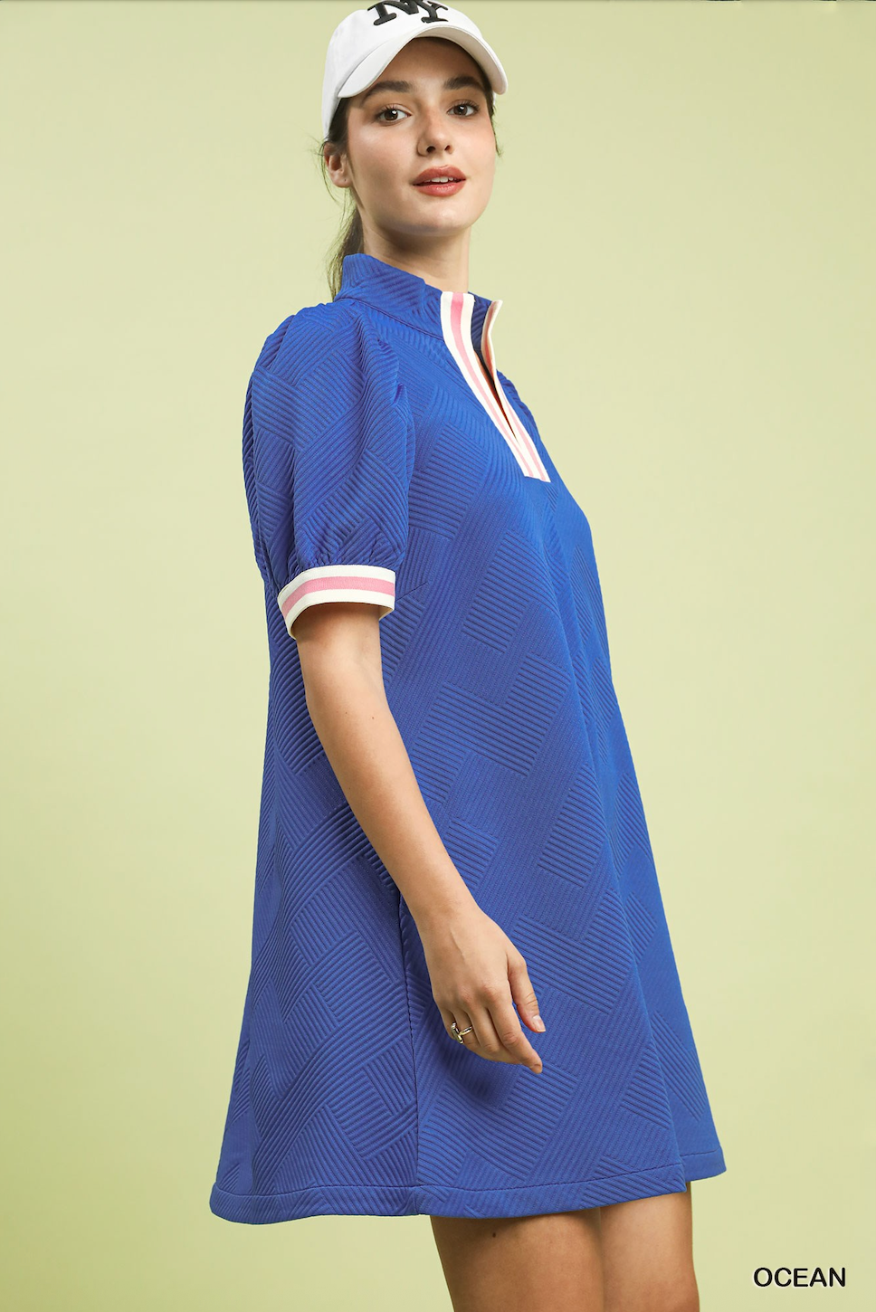 Woman wearing a blue dress with white collar and trim against a light green background