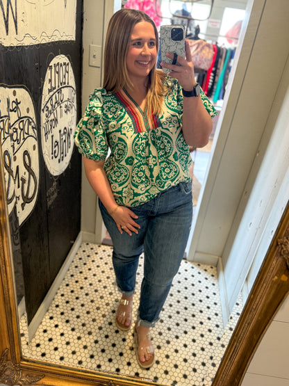 Woman taking a mirror selfie wearing a green patterned shirt and jeans in a store.