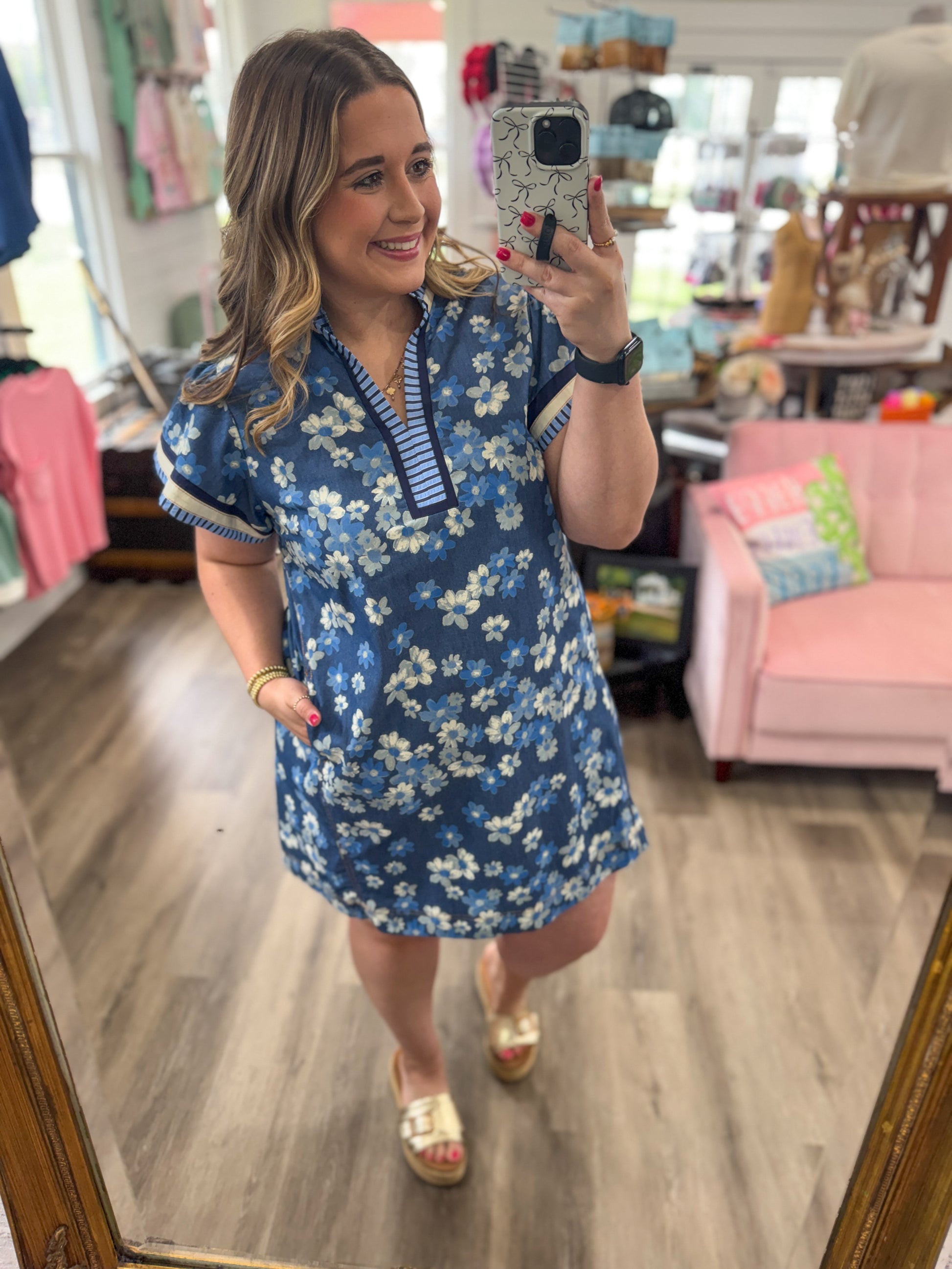 Woman taking a mirror selfie wearing a blue floral dress in a store.
