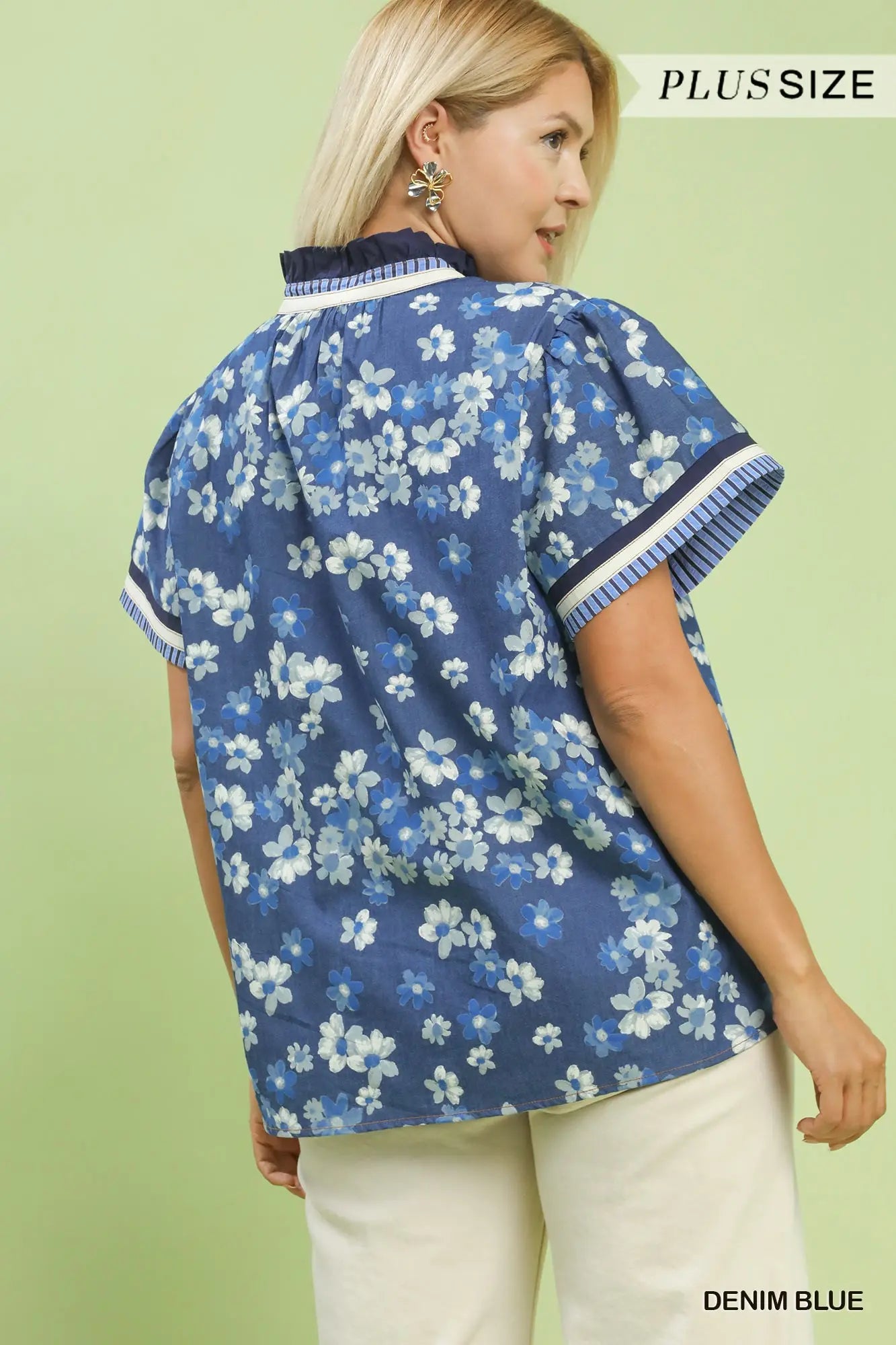 Woman wearing a blue floral blouse with white pants on a light green background