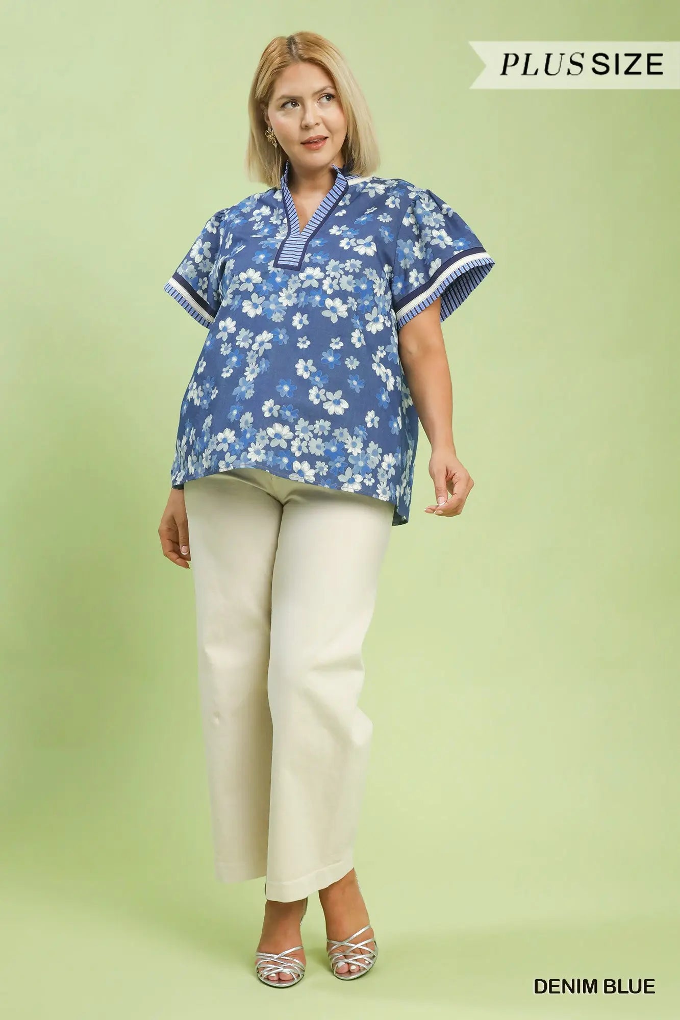 Woman wearing a blue floral blouse and white pants on a light green background