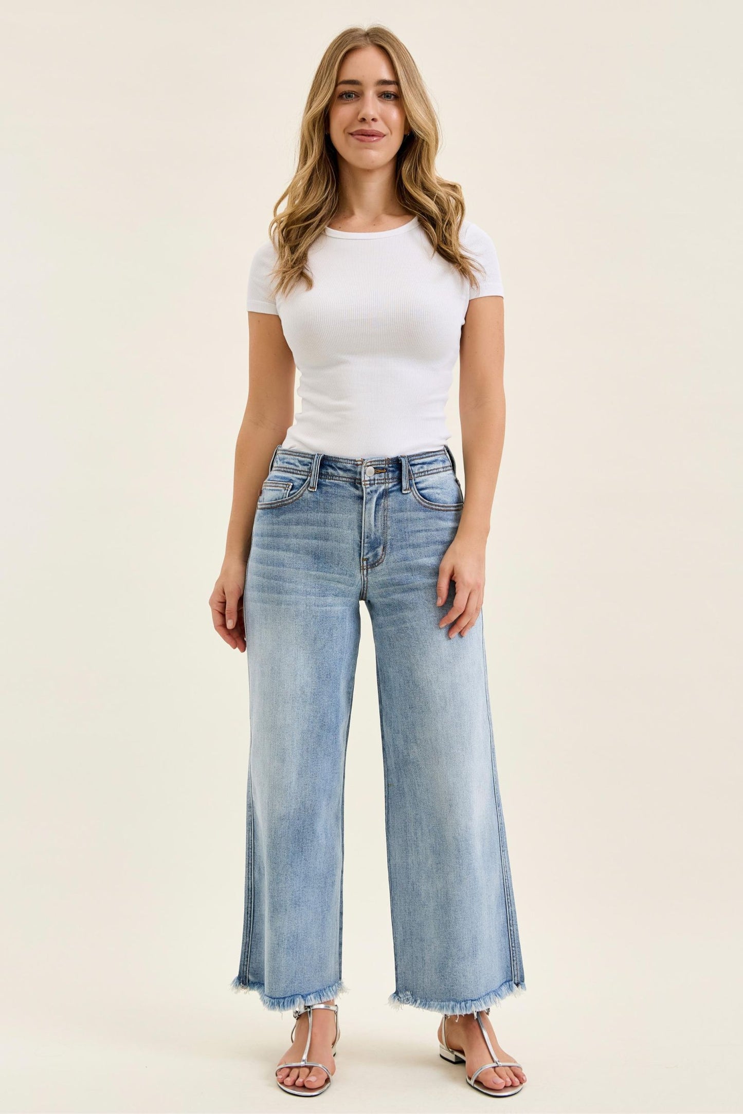Woman wearing a white t-shirt and light blue jeans on a beige background