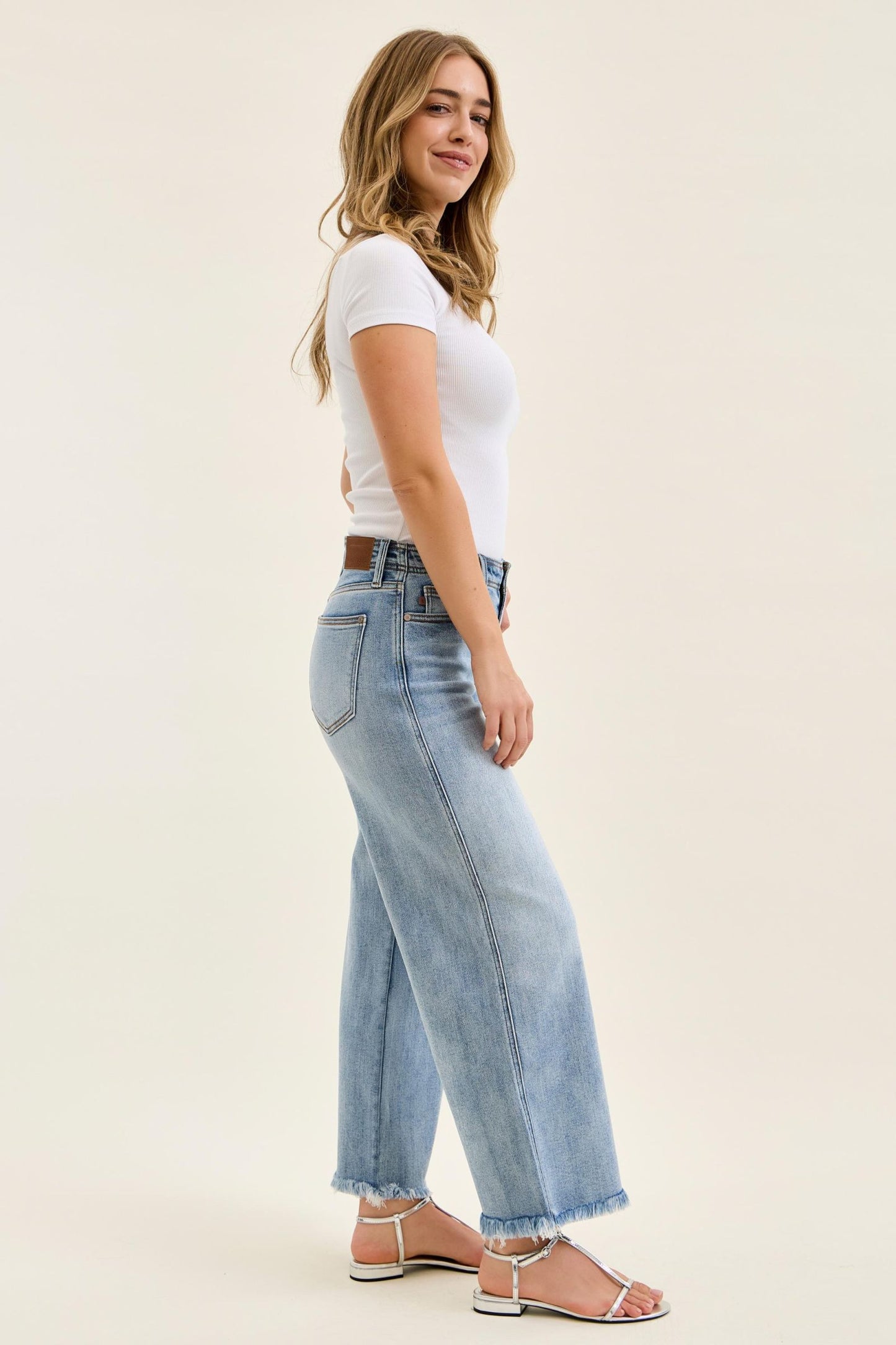 Woman wearing light blue jeans and a white top on a beige background