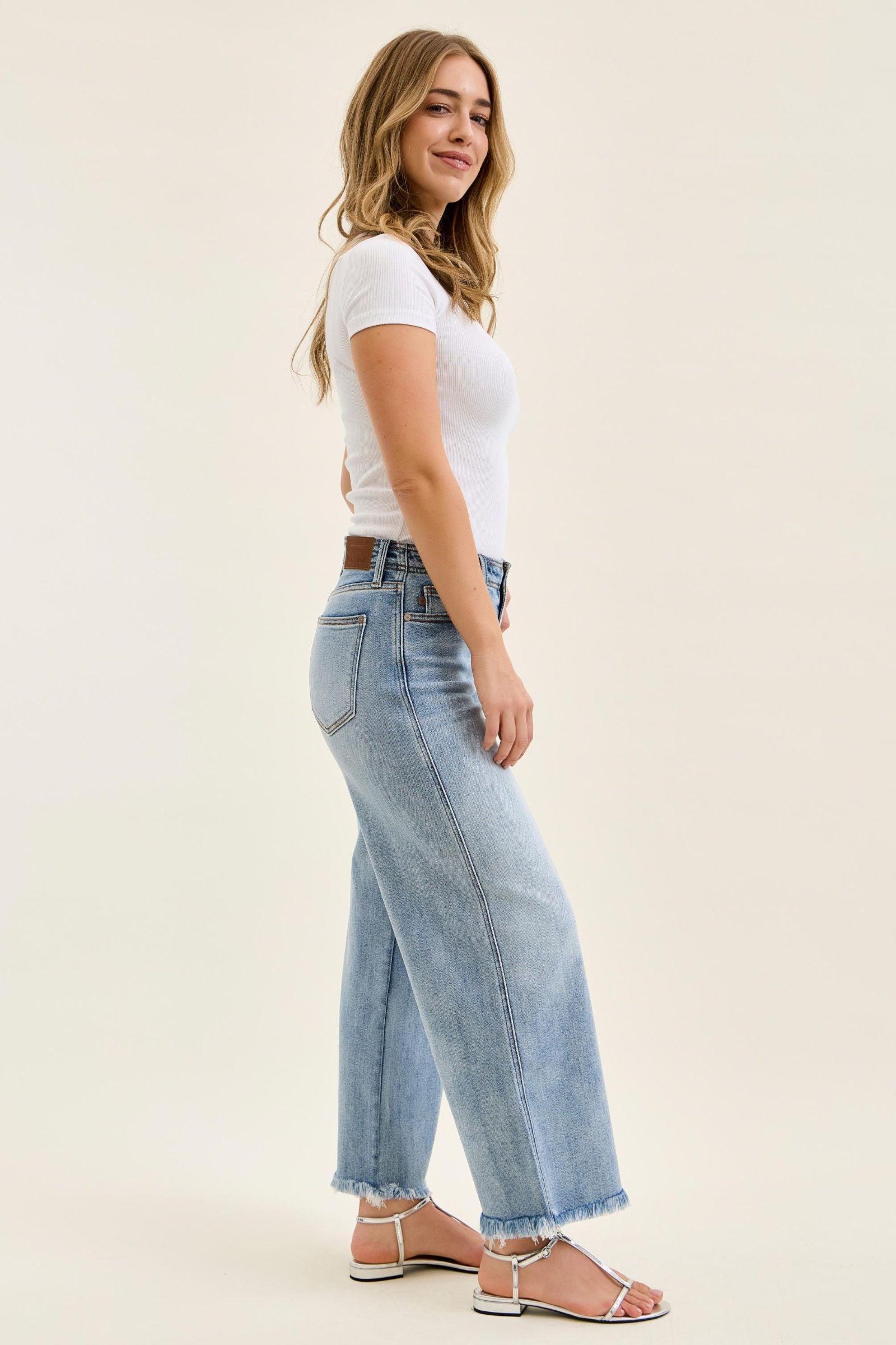 Woman wearing light blue jeans and a white top on a beige background