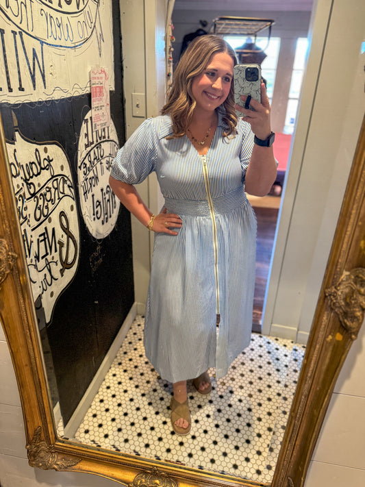 Woman taking a mirror selfie wearing a light blue dress in a room with decorative elements.