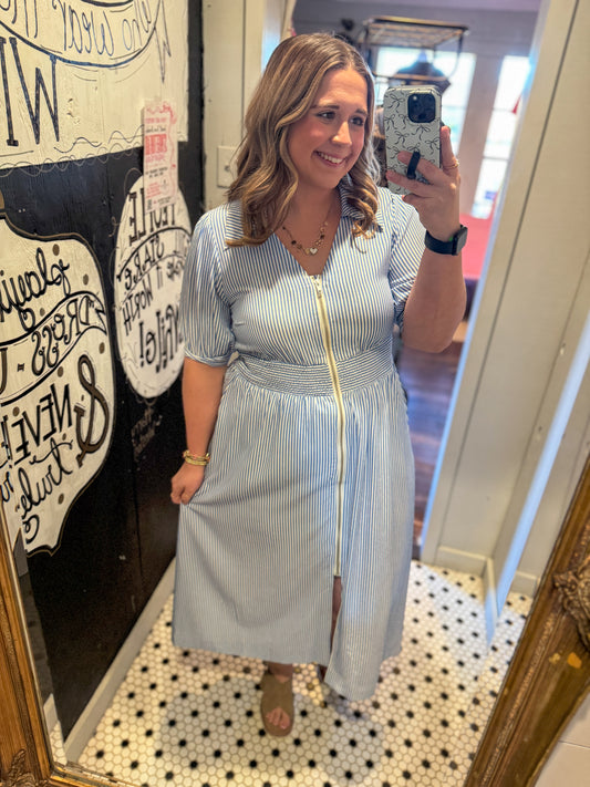Woman taking a mirror selfie wearing a blue and white striped dress in a store.