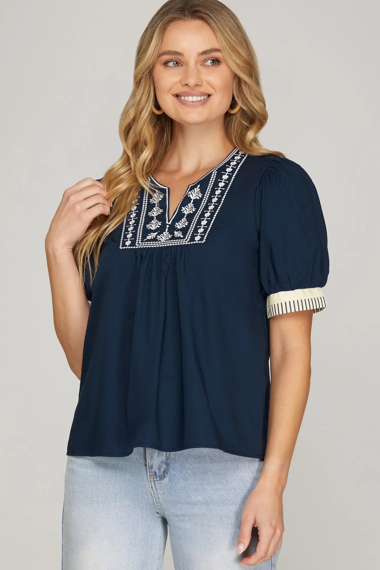 Woman wearing a navy blue blouse with white embroidery on a plain background